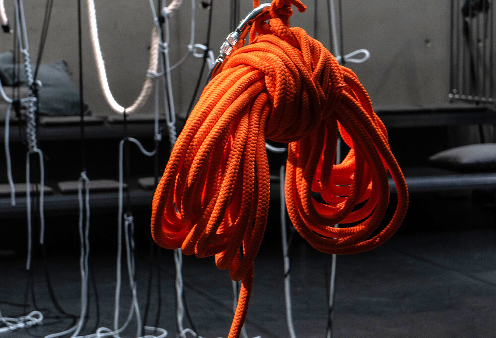 An orange knotted rope hangs in the room with other ropes
